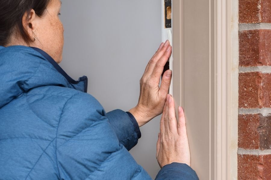 Homeowner applying fresh weatherstripping to an exterior door frame as part of storm preparation